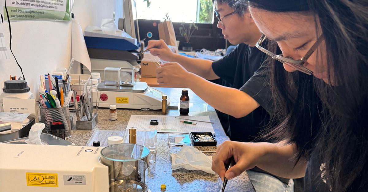 Foto von zwei Teilnehmer*innen der Summer School 2024 am Tisch beim Einwiegen von Proben, Foto von Wanqiong Mao